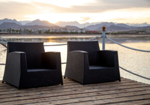 Two empty chairs on a wooden pier overlooking the mountains in the sunset light.